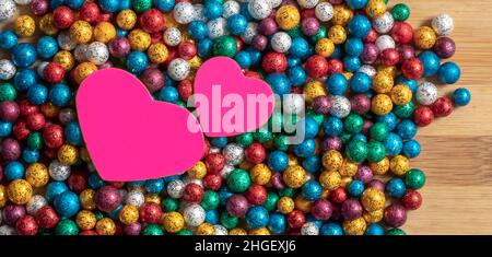 Valentine's Day backgrounds. Multicolor small size thermocol decorative balls with two pink hearts on top of a wooden table Stock Photo