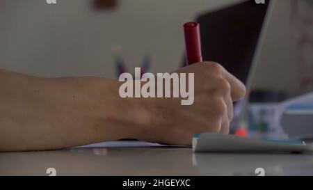 Close up side view of the table in the office with laptop and stationery and a hand drawing with red marker. Man hand drawing with red marker and taki Stock Photo