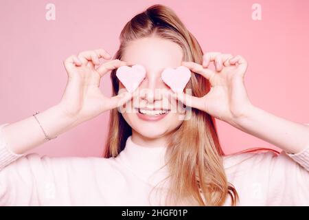 The girl closes her eyes with hearts, the girl is in love, Valentine's Day. The blonde on a pink background, surprised, excited, smiling, having fun. Stock Photo