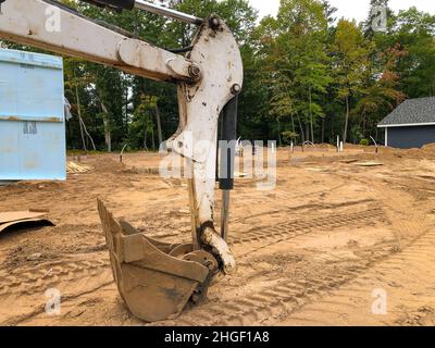 Backhoe scoop shovel attachment, used on excavator for moving soil or gravel, is resting on the dirt at a house construction site, near a pile of blue Stock Photo