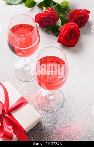 Two wine glasses with red wine for romantic dating or Valentine's day dinner with red rose on gray background. Vertical format. Stock Photo