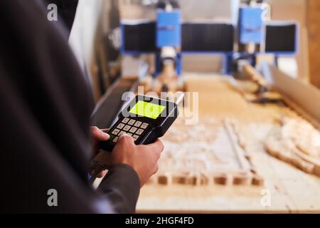 Hands close up holding the control panel of wood carving machine. Modern automatic woodworking machine with CNC. Furniture production. Stock Photo