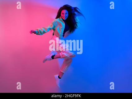 The brunette dances in neon, the dancer in red-blue. Hip hop girl, party, smile. Model in flight, jumping. Stock Photo