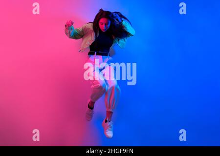 The brunette dances in neon, the dancer in red-blue. Hip hop girl, party, smile. Model in flight, jumping. Stock Photo