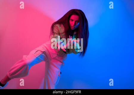 The brunette dances in neon, the dancer in red-blue. Hip hop girl, party, smile. Model in flight, jumping. Bright photo, emotions. Stock Photo