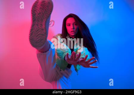 The brunette dances in neon, the dancer in red-blue. Hip hop girl, party, smile. Model in flight, jumping. Bright photo, emotions. Stock Photo