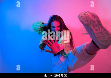 The brunette dances in neon, the dancer in red-blue. Hip hop girl, party, smile. Model in flight, jumping. Bright photo, emotions. Stock Photo