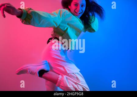 The brunette dances in neon, the dancer in red-blue. Hip hop girl, party, smile. Model in flight, jumping. Bright photo, emotions. Stock Photo