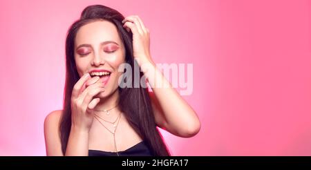 Girl eats macaroon, model on a pink background eats a sweet, sugar diet. Brunette with pink make-up, addicted to food. Place for text Stock Photo