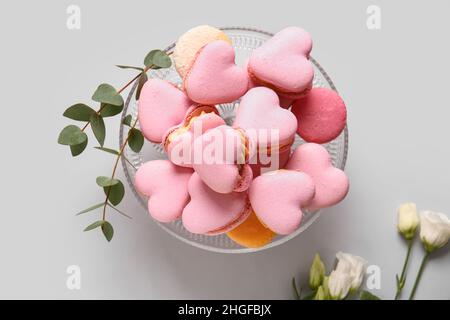 Dessert stand with tasty heart-shaped macaroons and flowers on grey background Stock Photo