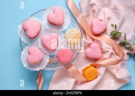 Dessert stand with tasty heart-shaped macaroons on blue background Stock Photo