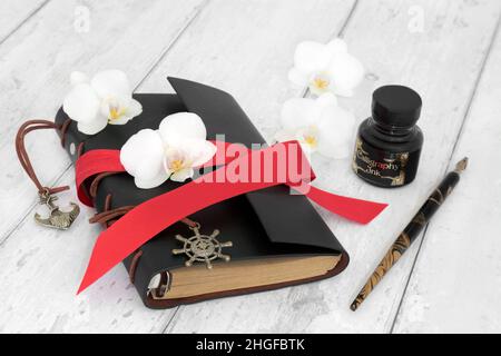 Old fashioned leather diary for personal notes, dream recording, thoughts and reminders with orchid flowers and nib pen with calligraphy ink bottle on Stock Photo
