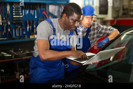 Two auto mechanics diagnosing car engine with laptop Stock Photo
