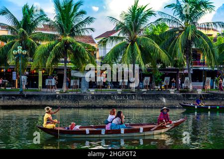 A small wooden tour boat goes down the Thu bon river carrying tourists by Old Town, Hoi An. Stock Photo