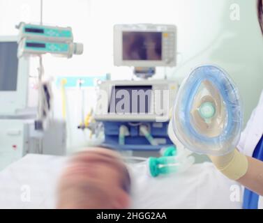 Female doctor holding oxygen mask in the gloved hands next to the patient in the bed. Stock Photo