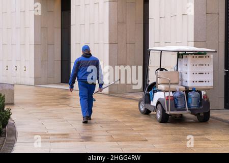 Man, park worker dressed in a blue work uniform with a net to remove leaves from the pool. Electric vehicle or golf car. Stock Photo