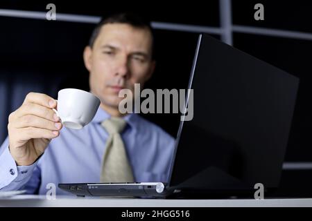 Coffee cup in hand of man sitting at laptop. Enjoying the hot drink, break during work in office Stock Photo