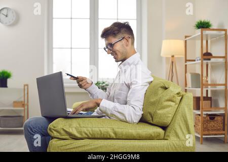 Young man sitting on couch at home and using laptop computer for work or studies Stock Photo
