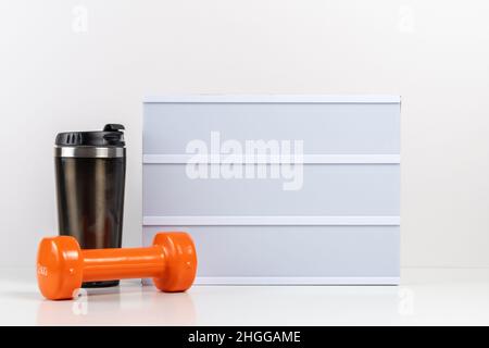 Fitness dumbbells with empty lightbox on white table. Mockup concept. Stock Photo