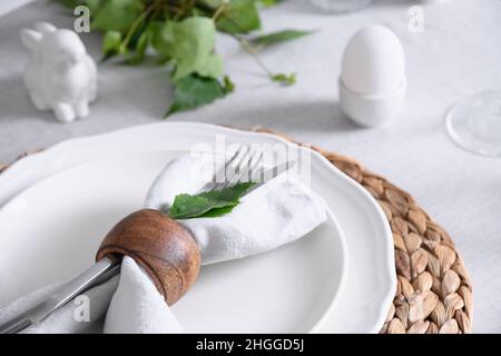 Easter table setting with yellow chick, festive decorations, fresh flowers and eggs on white tablecloth. Elegance dinner at home. Close up. Stock Photo