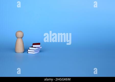 Education and knowledge concept. Wooden doll and pile of books on blue background with copy space Stock Photo