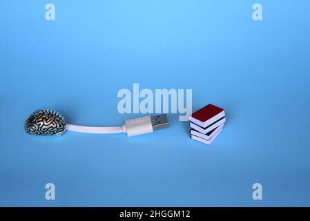 Study, learning, knowledge transfer concept. White cable, brain model and pile of books on blue background. Stock Photo