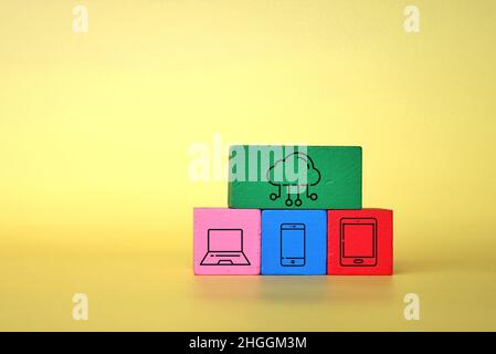 Technology and cloud computing concept. Wooden cubes with laptop, smartphone, tablet and cloud icon on yellow background. Stock Photo