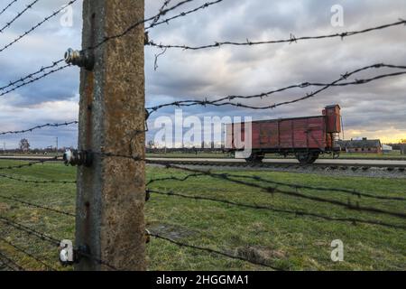 Barbed wire fence and an original railway carriage used for deportations at the former Nazi-German Auschwitz II-Birkenau concentration and extermination camp in Oswiecim, Poland on January 3, 2022. Stock Photo