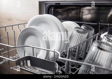 Front view of open automatic stainless fully integrated dishwasher range machine with clean utensils, cutlery, inside at modern home kitchen. Household domestic, kitchen appliances, lifestyle view Stock Photo