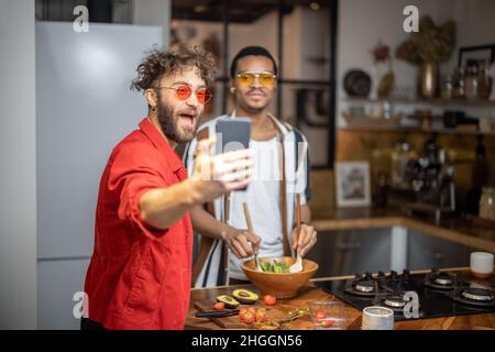 Two brightly dressed stylish guys taking selfie on phone indoors Stock Photo