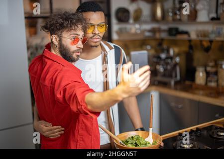 Two brightly dressed stylish guys taking selfie on phone indoors Stock Photo