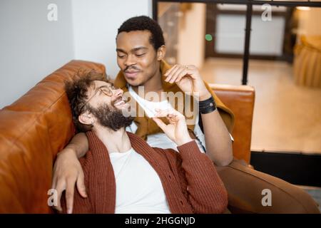 Male gay couple talking on a couch at home Stock Photo