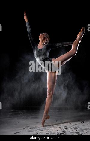 Dancing in flour concept. Pretty Gorgeous Ballerina woman dancer in dust fog. Portrait of female dancer in flour on black isolated backround, moving g Stock Photo