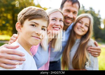Happy family with parents and two children hugging in the garden in summer Stock Photo