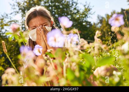 Girl blows her nose with hay fever or allergy in a flowering meadow Stock Photo