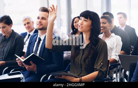 Cropped shot of an attractive young businesswoman sitting with her diverse colleagues and raising her hand while in the office Stock Photo