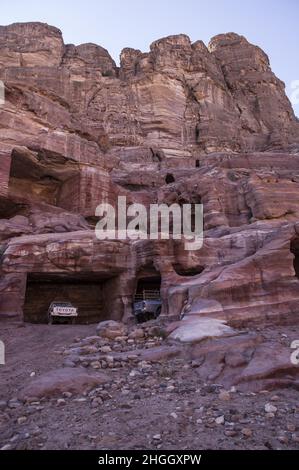 Toyota pickup trucks parked in ancient Nabatean structures in Petra, Jordan amid canyons, caves, desert landscape and buildings. Stock Photo