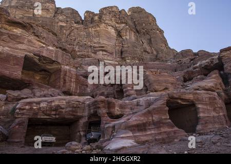Toyota pickup trucks parked in ancient Nabatean structures in Petra, Jordan amid canyons, caves, desert landscape and buildings. Stock Photo
