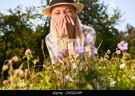 Woman with hay fever because of pollen allergy sits in a blooming summer meadow Stock Photo