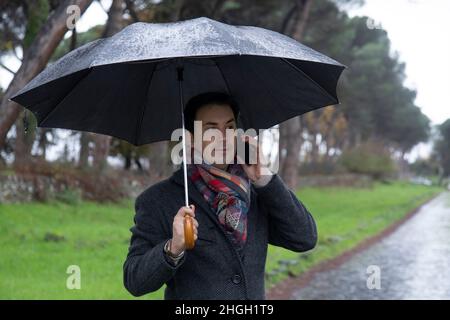 young  elegant man with umbrella talking on the phone in the rain Stock Photo