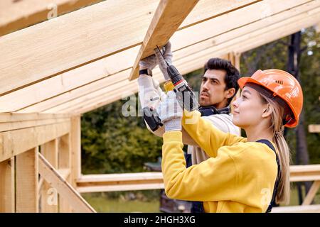 contractors in work wear using electric drill. Home renovation, sustainable living, building cottage house. Building Technologies. Industrial Theme. T Stock Photo