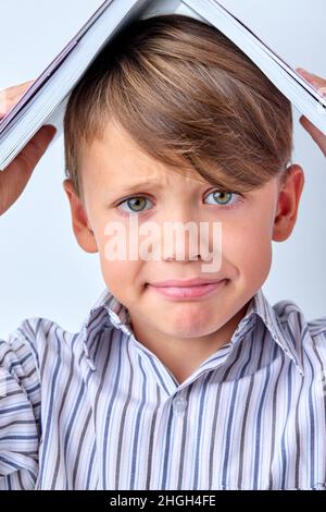 Close-up Caucasian School Child Boy Carrying Book on Head on White Studio Background, Copy Space. Sad Upset Kid Depressed By Going Back to School. Mot Stock Photo