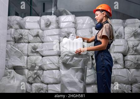 woman industrier packing Plastic barrels which contain in factory, preparing for sale. young female in blue uniform and orange hardhat. a lot of packe Stock Photo
