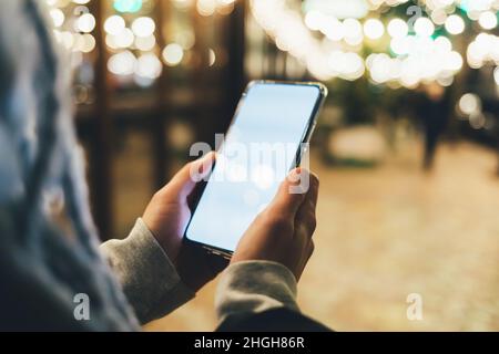 Close-up woman's hands holding modern smartphone with empty display on illuminated city street at night Stock Photo