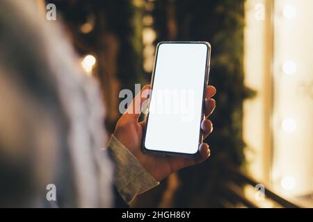 Woman's hand holding smartphone with blank screen outdoors in city in evening Stock Photo