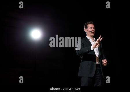 Guy speaking through microphone in dark conference hall, on stage, performance. Male in suit says about marketing and management for successful sales Stock Photo