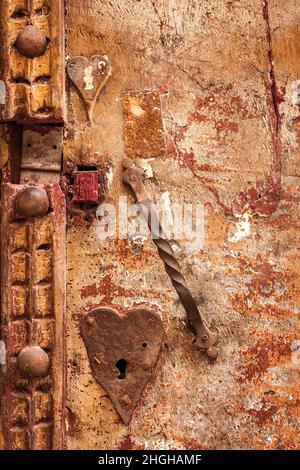 Old ornate weathered red painted door detail with metal handle and heart shaped metal key hole Stock Photo