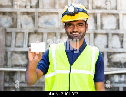 Happy smiling young electrician or repairman showing white job card by looking at camera - conncept of repair service, advertisment and promotion. Stock Photo