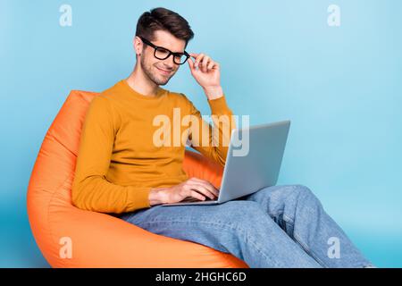 Portrait of attractive focused cheery guy sitting in chair using laptop writing e-mail isolated over bright blue color background Stock Photo