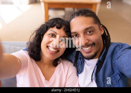 Portrait of smiling young multiracial couple taking selfie together at home Stock Photo